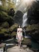 A woman in a white bikini standing in front of a waterfall.