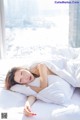 A woman laying on a bed with white sheets and pillows.