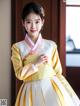 A woman in a yellow and white hanbok poses for a picture.