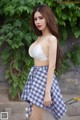 A woman in a white bra top and plaid skirt posing for a picture.